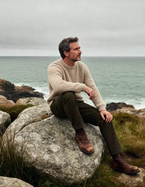 Uomo con maglione in maglia seduto su uno scoglio in riva al mare