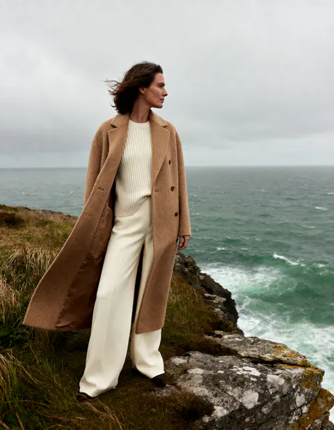 Donna con cappotto cammello vicino a una scogliera